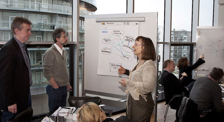 Tre personer står foran tavle og taler sammen