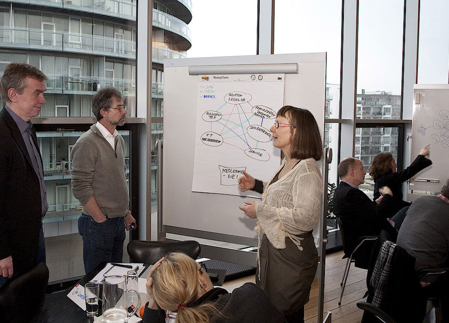 Tre personer står foran tavle og taler sammen